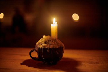 Tek bir mum, loş ışıklı odadaki sade ahşap masada parlak bir şekilde yanarak sıcak ve huzurlu bir atmosfer yaratır. Eski bir meyhane masasında mum, eski bir meyhanenin çekiciliğini çağrıştırıyor, sakin bir ortam.