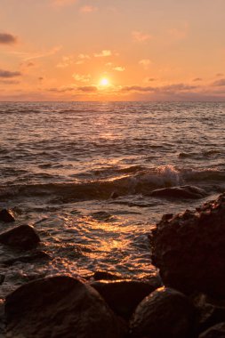 Uçsuz bucaksız okyanus üzerinde sakin bir gün batımı, yumuşak dalgalar ve kayalık kıyı şeritleri üzerine altın renkler döküyor. Sakinleştirici ortam yansımayı ve barışı davet eder.