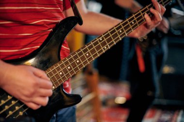 Müzisyen elinin performans sırasında bas gitar çalmasına odaklanmış bakış açısı, loş ortamda telleri ve perdeleri vurgulamak, yeni grup üyesi için müzikal prova