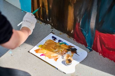 Yetişkinlerin el boyamasına odaklanmış bir manzara. Eldivenli el fırçası, pürüzsüz yüzeyde hassas ve sanatsal bir şekilde canlı kırmızı ve mavi renkler uygular.