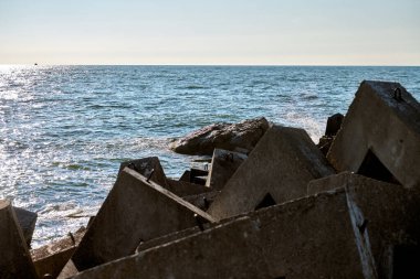 Büyük beton bloklar kıyı dalgaları oluşturarak okyanus dalgalarına karşı koruyucu bariyer oluşturur. Serin mavi gökyüzü deniz kenarının huzurlu atmosferini arttırır.
