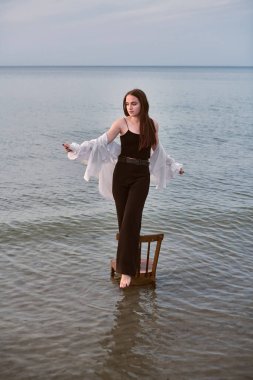 Genç kadın sakin ve sığ deniz sularına batmış bir şekilde sandalyede kendinden emin bir şekilde duruyor. Gündelik giysiler içinde uçsuz bucaksız ufukta sükûnet saçar. Yansıma denge ve içgözlem anlamına gelir.