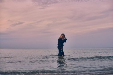 Genç kadın Pastel gökyüzünün altında sakin denizde tek başına yürüyor. Onun rahatlatıcı okyanus zeminine karşı düşünceli duruşu içgözlem ve huzuru çağrıştırıyor.