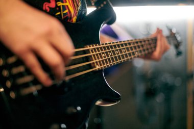Müzisyen elinin performans sırasında bas gitar çalmasına odaklanmış bakış açısı, loş ortamda telleri ve perdeleri vurgulamak, yeni grup üyesi için müzikal prova