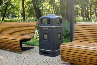 Huzur parkındaki ahşap banklar ve modern çöp kutuları, canlı yeşilliklerle çevrili konfor ve temizlik sunuyor. Rahatlamak için mükemmel.