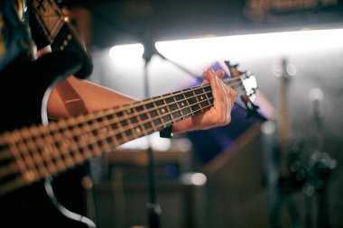 Müzisyen elinin performans sırasında bas gitar çalmasına odaklanmış bakış açısı, loş ortamda telleri ve perdeleri vurgulamak, yeni grup üyesi için müzikal prova