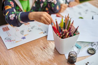 Çocuk ahşap yüzeyde renkli çizimler yapıyor. Odaklanan parlak kalemler. Doğal ışık arttırıcı yaratıcılığa sahip sıradan bir iç mekan