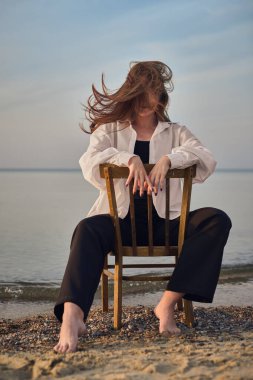 Genç kadın sakin denize bakan sandalyede oturuyor, yalnızlığı ve içyüzünü simgeliyor. Rahat duruşu ve dalgalı saçları, alacakaranlıkta sakin ve düşünceli bir ruh halini çağrıştırıyor.