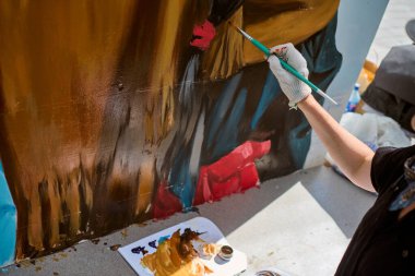 Yetişkinlerin el boyamasına odaklanmış bir manzara. Eldivenli el fırçası, pürüzsüz yüzeyde hassas ve sanatsal bir şekilde canlı kırmızı ve mavi renkler uygular.