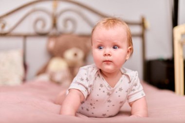 Açık renk saçlı, neşeli yüzlü, yıldız desenli pijamalı bir kız çocuğu. Pembe yatak, bulanık ayıcık arka plan, yumuşak ışıklandırma, rahat ev dekorasyonu, sıcak atmosfer.