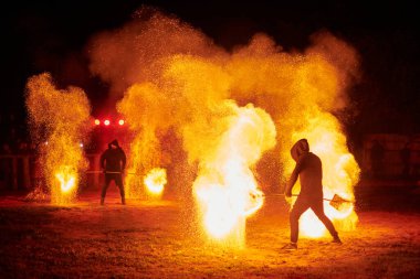 Gece gökyüzünde parıldayan iki itfaiyeci silueti, bir yangın gösterisi sırasında enerji ve ateş manipülasyonu gösteriyorlar.