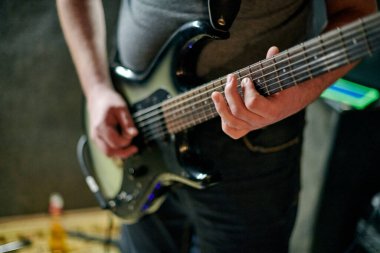 Müzik provasında elektro bas gitar çalan müzisyen, loş ayarlarda gitar tekniği pratik yapan, gitarist ellerini kapat