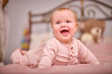 Açık renk saçlı, beyaz ırktan, pembe elbiseli, neşeli genç bir kadın. Ilık aydınlatma neşeli ifadeyi artırır. Yumuşak dekor samimi dokunuş ekler