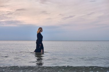 Siyah elbiseli genç bir kadın alacakaranlıkta sakin okyanus sularında yürür, yalnızlığı ve yansımayı somutlaştırır. Onun sakin tavırları deniz ve gökyüzünün durgunluğunu yansıtıyor.