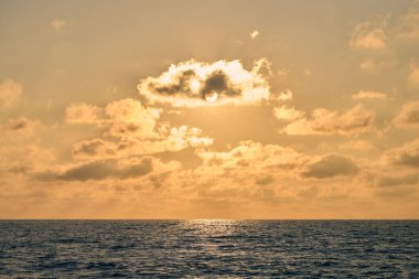 Huzurlu altın günbatımı, huzurlu okyanus ufkunun üzerinde sıcak bir ışık saçar ve sakin bir ortam yaratır. Yumuşak güneş ışınları dağınık bulutları delip geçer, sakinlik ve içgözlem çağrıştırır