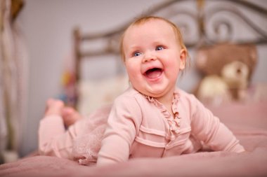 Açık renk saçlı, beyaz ırktan, pembe elbiseli, neşeli genç bir kadın. Ilık aydınlatma neşeli ifadeyi artırır. Yumuşak dekor samimi dokunuş ekler