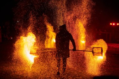 Gece gökyüzünde parıldayan iki itfaiyeci silueti, bir yangın gösterisi sırasında enerji ve ateş manipülasyonu gösteriyorlar.