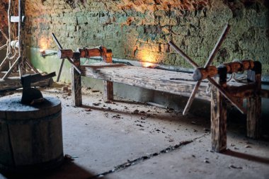 Ahşap ortaçağ işkence rafı, taştan duvarlarla çevrili zindanlar, loş ışıklandırmayla aydınlatılmış, tarihsel zalimliğin acımasız hatırlatıcılarını sembolize ediyor.