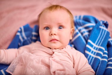 Açık kahverengi saçlı, açık tenli, yumuşak mavi ekose battaniyede dinlenen bir bebek kadın. Hafif ışıklandırma ayarında hafif şaşırmış ifade