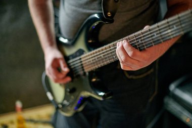Müzik provasında elektro bas gitar çalan müzisyen, loş ayarlarda gitar tekniği pratik yapan, gitarist ellerini kapat