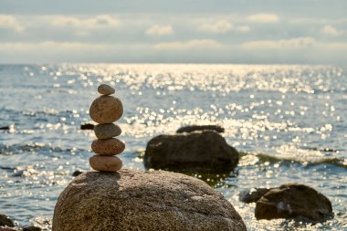 Sakin deniz kıyısında kayaların üzerinde dengelenmiş pürüzsüz taşlar yığını, denge ve sükuneti sembolize eder, barışçıl ve meditasyonel atmosferi çağrıştırır.