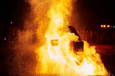 Gece gökyüzünde parıldayan iki itfaiyeci silueti, bir yangın gösterisi sırasında enerji ve ateş manipülasyonu gösteriyorlar.