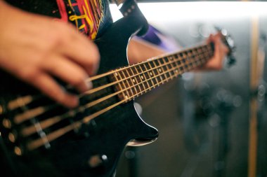 Müzisyen elinin performans sırasında bas gitar çalmasına odaklanmış bakış açısı, loş ortamda telleri ve perdeleri vurgulamak, yeni grup üyesi için müzikal prova