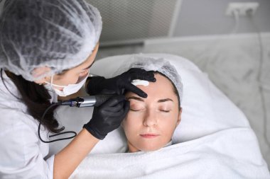 Profesyonel kaş makyajı, temiz, sakin bir spa ortamında, hassas ve dikkatli bir şekilde rahatlamış yetişkin bir kadın üzerinde uygulanır. Serene ayarı konfor ve güveni çağrıştırıyor, üst görünüm