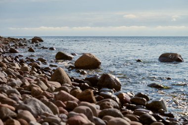 Kıyı şeridi sakin okyanusa doğru uzanır ve pürüzsüz taşlar kıyı boyunca dağılır. Yumuşak dalgalar rahatlatıcı bir ortam yaratır. Huzurlu ve sakin bir atmosferi yansıtır.