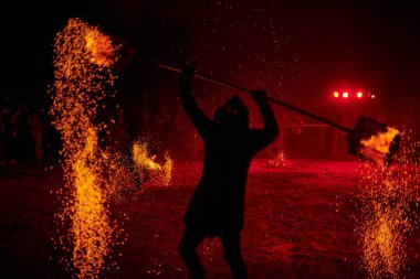 Gece gökyüzünde parıldayan iki itfaiyeci silueti, bir yangın gösterisi sırasında enerji ve ateş manipülasyonu gösteriyorlar.