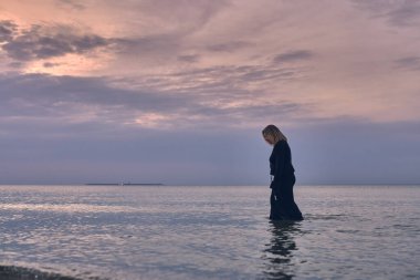 Siyah elbiseli genç bir kadın sakin okyanus sularında gün batımında yürüyor. Gökyüzünün pembe renkleri yalnızlık ve huzur duygusunu çağrıştırıyor, içselliği sembolize ediyor