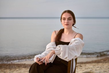 Derin düşüncelere dalmış genç bir kadın sanatçı sakin bir okyanusun kenarında oturur. Onun sakin ifadesi ve yumuşak ışıklandırması huzur ve içgözlem duygusunu çağrıştırıyor.