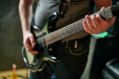 Müzik provasında elektro bas gitar çalan müzisyen, loş ayarlarda gitar tekniği pratik yapan, gitarist ellerini kapat