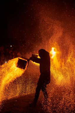 Gece gökyüzünde parıldayan iki itfaiyeci silueti, bir yangın gösterisi sırasında enerji ve ateş manipülasyonu gösteriyorlar.