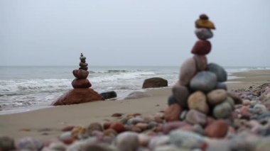 Dengeli taş kuleler bulutlu gökyüzünün altında sakin kumsalları süsler. Yumuşak dalgalar kıyı şeridini kaplıyor, sakin ve meditasyon havası yaratıyor. Gri ve toprak renklerinin soluk tonları sahneye hakim