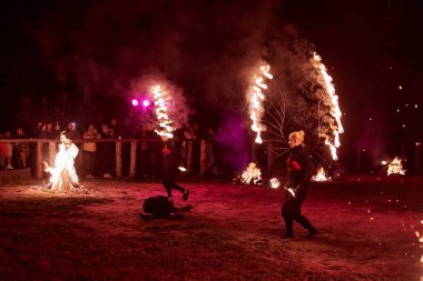 Kaliningrad, Rusya - 10.09.2022 - İki kadın ateş gösterisi sanatçısı koyu arka plana karşı alevli ateş kanatları ile, canlı performans yoğunluğu ve heyecanı yakalıyor