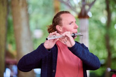 Kaliningrad, Russia - 10.08.2024 - Adult male musician playing clarinet outdoors. Natural light, blurred green background, side profile, focused expression clipart