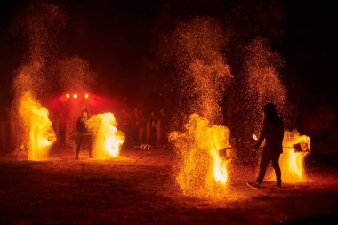 Kaliningrad, Rusya - 10.09.2022 - Işıl ışıl iki itfaiyecinin silueti gece gökyüzünde parlıyor, bir açık hava yangın gösterisi sırasında enerji ve ateş manipülasyonu sanatını sergiliyor