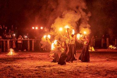 Kaliningrad, Rusya - 10.09.2022 - Muhteşem gece gösterisinde otantik bir elbiseyle dans eden ateş gösterisi sanatçıları, gece gökyüzü altında ateşli hareketler, izleyiciler