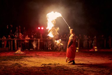 Kaliningrad, Rusya - 10.09.2022 - Tanrı 'nın tarihi kostümlü ateş sanatçısı seyircilerin önünde ateşli asasını sallıyor, dramatik kırmızı ışık çarpıcı, dünyevi bir parıltı yaratıyor