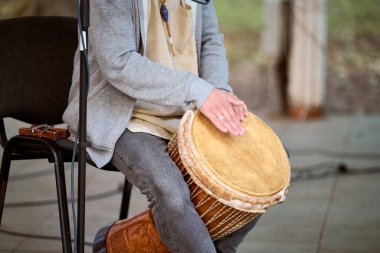 Kaliningrad, Rusya - 10.08.2024 - parkta djembe oynayan genç bir adam. Günlük kıyafetler, rahat bir hava. Doğal ışık, arka plandaki yeşillik sahneyi güçlendirir