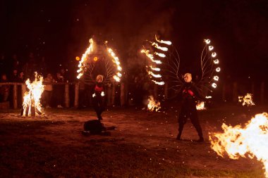 Kaliningrad, Rusya - 10.09.2022 - İki kadın ateş gösterisi sanatçısı koyu arka plana karşı alevli ateş kanatları ile, canlı performans yoğunluğu ve heyecanı yakalıyor
