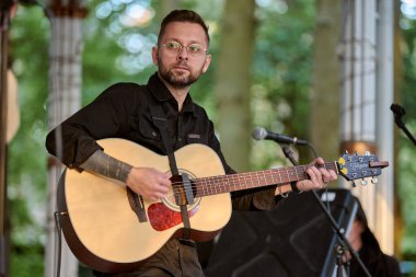 Kaliningrad, Rusya - 10.08.2024 - Genç adam akustik gitar çalıyor. Huzurlu doğal arkaplan sanatsal ortamı geliştirir