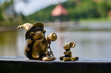 Svetlogorsk, Rusya - 13.07.2024 - Garip bronz kirpi şapkalı büyücü teleskop, yanında da manzaralı göl manzaralı biblo