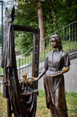 Svetlogorsk, Rusya - 13.07.2024 - Kitaplı zarif bronz heykel, kumaşlı ve dekoratif çerçeveli kedi, açık havada Svetlogorsk parkında, kedi heykeli olan kadın ressam