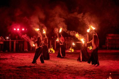 Kaliningrad, Rusya - 10.09.2022 - Muhteşem gece gösterisinde otantik bir elbiseyle dans eden ateş gösterisi sanatçıları, gece gökyüzü altında ateşli hareketler, izleyiciler