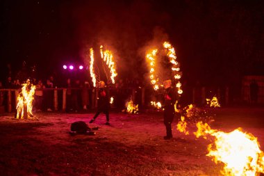 Kaliningrad, Rusya - 10.09.2022 - İki kadın ateş gösterisi sanatçısı koyu arka plana karşı alevli ateş kanatları ile, canlı performans yoğunluğu ve heyecanı yakalıyor