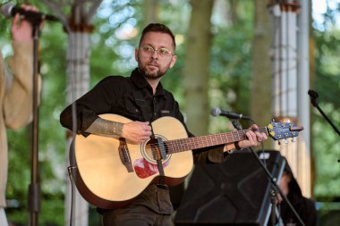 Kaliningrad, Rusya - 10.08.2024 - Genç adam akustik gitar çalıyor. Huzurlu doğal arkaplan sanatsal ortamı geliştirir