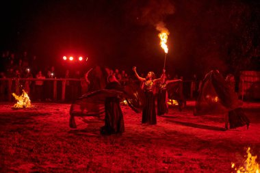 Kaliningrad, Rusya - 10.09.2022 - Muhteşem gece gösterisinde otantik bir elbiseyle dans eden ateş gösterisi sanatçıları, gece gökyüzü altında ateşli hareketler, izleyiciler