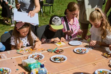 Kaliningrad, Rusya - 10.08.2024 - açık mozaik atölyesinde çeşitli çocuklar güneşli bir günde sanat yaratmakla meşguller. Renkli karolarla kaplı bir masa
